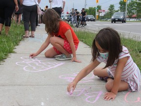 Ella Zadorsky-Hall, 5, (front) and Nyah Smith, 8, paint hearts on the sidewalk of Hyde Park Road on Tuesday night. They were among scores of Londoners who joined together to mourn four members of a local Muslim family killed in what police call a hate-motivated crime. (JONATHAN JUHA/The London Free Press)