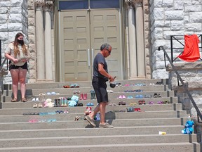 George Couchie and his granddaughter, Grace Couchie, smudge the pairs of shoes, Tuesday, placed at the Pro-Cathedral of the Assumption in North Bay for the 215 children whose graves were found at a former residential school in British Columbia. Michael Lee/The Nugget