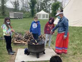 Elder Lorraine Albert of the Mikisew Cree First Nation cooks bannock over a fire with children at a FMPSD land-based learning camp on Monday, June 21, 2021. Supplied Image/Annalee Nutter/FMPSD