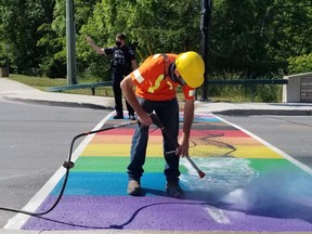 City worker Mark Vachon attempts to remove black paint discovered on the newly painted rainbow crosswalk Sunday morning in Owen Sound, Ont. Const. Chris Mahy directs traffic around him. (Scott Dunn/The Sun Times/Postmedia Network)