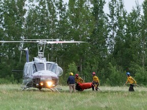 Alberta wildland firefighters work with a helicopter as they battle a wildfire between Evansburg and Wildwood on Tuesday, June 22, 2021. The pilot of a helicopter that crashed while fighting a wildfire near Evansburg has died.