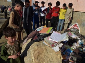 Onlookers stand next to the backpacks and books of victims following multiple blasts outside a girls' school in Dasht-e-Barchi on the outskirts of Kabul on May 9, 2021, as the death toll has risen to 50, the interior ministry said. (Photo by WAKIL KOHSAR / AFP)