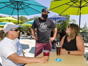 Flux Brewing Co. co-owner Jeremy Hansen (centre) chats with Brent and Courtney Kay of Waterford on the patio of the craft brewery near Scotland as the province on Friday entered Step One of its pandemic reopening plan.