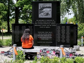 A visitor sits at the Walpole Island First Nation monument dedicated to the children from the community who attended Indigenous residential schools. Dozens of pairs of children's shoes were dropped off at the monument Monday. Mark Malone