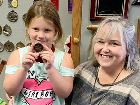 Ivy Kennedy, 5, holds up a medal next to her aunt, Corrinne Kennedy, owner of Rubies Inc. in Chatham. The gift shop is awarding medals to elementary school children free of charge.