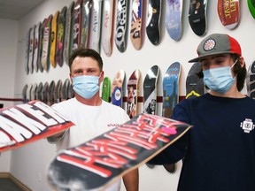 Cory Cowan, left, and his son Avery, 17, hold out two skateboard decks in front of the board wall at their business, Family Skateboard Company, in downtown Chatham June 23, 2021.