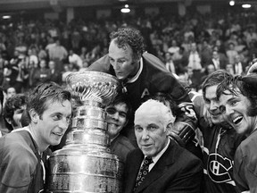 Montreal Canadiens' Henri Richard, centre, who scored the game-winning goal, peers into the Stanley Cup held by team captain Jean Béliveau, left, and NHL Commissioner Clarence Campbell in Chicago, on May 18, 1971.