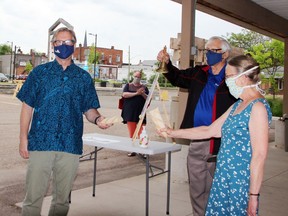 Pembroke Mayor Mike LeMay rings the bell to signal the official opening of the Pembroke Farmers' Market for the 2021 season. Looking on are Pembroke Coun. Brian Abdallah, the city's representative on the market board and market volunteer Linda Dyck, who are each holding a baguette half after the mayor sliced the loaf instead of cutting a ribbon to open the market.
