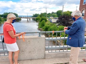 Pembroke Coun. Christine Reavie and Mayor Mike LeMay tie orange ribbons around the railing of the Pembroke Street Bridge near city hall during a ceremony June 28 with residential school survivors and their families.
