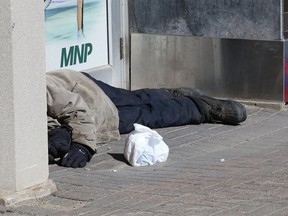 A man rests at an entrance to the Sudbury Community Arena on March 12, 2021. Northern Ontario's mayors say they need help dealing with the opioids crisis and the related problem of homelessness.