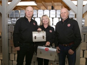 Doug Patrick, left, and his brother, Steve, of L. May Mfg., look on as Catherine Langin, of L. May Metal Fabricators Ltd., displays old and new metal lunchboxes in Sudbury on May 13.