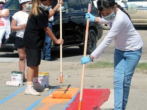 Victoria Swampy (front) and Tisean Redcalf get started on repainting the rainbow crosswalk at Samson Cree Nation Saturday following a small ceremony.