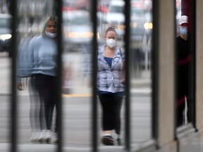 People wearing masks are reflected in a row of windows in Winnipeg on Friday, June 11, 2021.