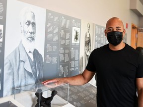Steven Cook, site manager at Uncle Tom's Cabin Historic Site in Dresden, is shown next to a photo of Josiah Henson inside the museum July 21, 2021. (Tom Morrison/Chatham This Week)