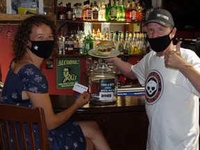 Bob Firth (right) holding one of his ThunderCrunch burgers next to a patron filling out a raffle form for the initiative. A part of all proceeds will go toward the CMHA Kenora Branch.