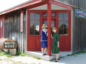 Grey Roots engagement students Sydnie Walker, left, and Gillian Wagenaar stand in front of Moreston Heritage Village's Bluewater Garage Wednesday while dressed in heritage costumes. Grey Roots is set to open outdoor spaces in the pioneer village Friday. DENIS LANGLOIS