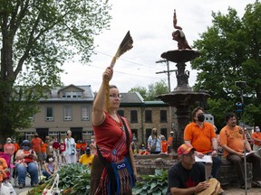 A sea of orange fills the grounds of Gananoque Town Hall  on Canada Day during  a memorial to reflect on the hundreds of unmarked gravesites that have been found across Canada. Clarice Gervais holds eagle feathers in the air while Donna Lynn Neil tells her story of her life and the hardships she has faced as an Indigenous person. (JESSICA MUNRO/Local Journalism Initiative)