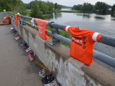 A row of shoes and moccasins, along with Every Child Matters shirts, line the bridge leading to the Atikameksheng First Nation in memory of residential school victims.