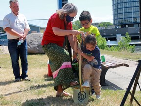 Kenora Rotary Peace Park co-chair Kelly Williams, left, gets some help from six-year-old Lynkston LeDoux-DeBungee, middle, and four-year-old Kyson DeBungee of Rainy River First Nation as Kenora's director of community services Stace Gander looks on to officially break the ground at the Rotary Peace Park on First Avene South following the blessing of the land on Friday, July 11.