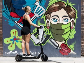 A woman rides an e-scooter past a pandemic themed mural on Rideau Street in Ottawa on Tuesday, Jun. 8, 2021. (ERROL MCGIHON, Postmedia Network)