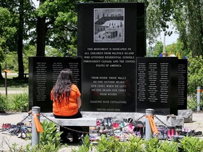 A visitor sits at the Walpole Island First Nation monument dedicated to the children from the community who attended Indigenous residential schools. Dozens of pairs of children's shoes were dropped off at the monument. Mark Malone