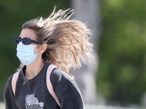 A person wears a mask and sunglasses while crossing a street on a windy day in Winnipeg on Wednesday. Chris Procaylo/Winnipeg Sun