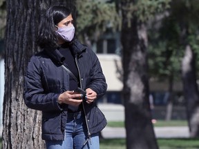 A woman wearing a mask waits for her ride on Broadway in Winnipeg on Tues., Aug. 25, 2021.