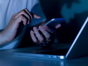 close up young man hand holding smartphone for access by unlock on screen and using laptop for register website on internet in the late night , internet addiction concept