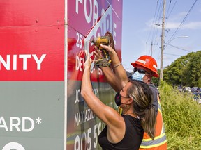 Norfolk County mayor Kristal Chopp gets help from roads foreman Mike Evans affixing a "Sold" banner on a real estate sign for the 25-acre HUB lands on Ireland Road in Simcoe on Friday September 3, 2021.