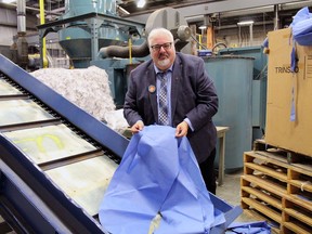 Andy Straisfeld, a partner in LifeCycle Revive and the company's vice-president of business development, gets ready to feed a medical gown into a shredder at the grand opening of the plant on Wednesday. The company, located on Plant Farm Boulevard, converts used personal protective equipment into reusable polypropylene plastic pellets.