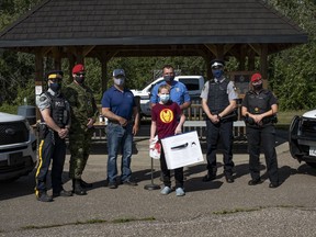 The Military Police, Royal Canadian Mounted Police and Cold Lake Peace Officers reward youth in the community for practicing safety during the summer at 4 Wing Cold Lake, Aug. 20, 2021.  (Left to right backrow) Const. Andrew Kary, Corporal Collin Hickey, Warren Hobart, David Zimmerman, CPO Simon Crevier and Sgt. Angie Castle.  (Front row) Simon Hare.   Photo: Cpl Connie Valin/ 4 Wing Imaging