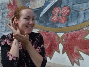 Sara Racine poses while wearing one of her poppy earrings beside the mural at the Royal Canadian Legion Branch 296, on Saturday August 7, 2021 in Cornwall, Ont. Shawna O'Neill/Cornwall Standard-Freeholder/Postmedia Network