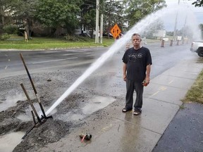 Arthur Milnes gets an unexpected morning shower with his coffee as he stands in the water streaming from a burst temporary municipal water pipe outside his Johnson Street home on Sunday morning.