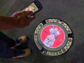 A passerby takes a photo of an illuminated manhole cover, with designs of popular animation character Gundam, on the street in Tokorozawa, near Tokyo.