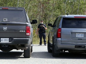 An OPP officer is framed by two police vehicles near a roadblock set up at Kukagami Lake Road and Highway 17 east of Sudbury, Ont. on Sept. 2.