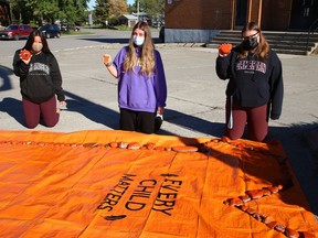 Grade 12 students Sharlah Nebenionquit, left, Brooke Moneweg and Katie Punkari placed painted orange rocks with messages on a tarp representing an orange T-shirt at Lively District Secondary School on Sept. 29. The activity was one of a number of events students participated in this week as part of the National Day for Truth and Reconciliation. City councillors showed their support Tuesday by wearing orange T-shirts to their council meeting.