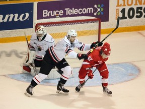 Owen Sound Attack defenceman Mark Woolley cross checks Soo Greyhounds forward Justin Cloutier while Mack Guzda takes a shot to the logo as the Attack hosted the  Greyhounds at the Harry Lumley Bayshore Community Centre in Owen Sound on Saturday night. The Attack picked up a 5-3 victory over the Hounds.