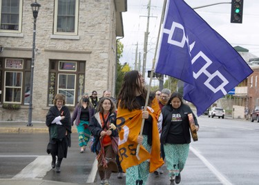 Kiki Olivier carries the Great Law of Peace flag while leading a group of people from the bandstand in Town Park to the end of Stone Street South during a Water Walk. The walk led the group down to a plot of land where the park was declared the First Peoples Park of the Thousand Islands during the First Peoples Performing Arts Festival. (JESSICA MUNRO/Local Journalism Initiative)