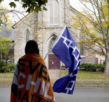Kiki Olivier looks out to St. Andrew's Presbyterian Church during a Water Walk and waves the Great Law of Peace flag. (JESSICA MUNRO/Local Journalism Initiative)