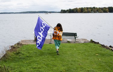 Kiki Olivier carries the Great Law of Peace flag while leading a group of people from the bandstand in Town Park to the end of Stone Street South during a Water Walk. The walk led the group down to a plot of land where the park was declared the First Peoples Park of the Thousand Islands. (JESSICA MUNRO/Local Journalism Initiative)