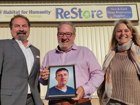 Holding a portrait of late Intelligencer journalist Dave Vachon, Habitat for Humanity Prince Edward-Hastings executive director Hazzem (Hank) Koudsi, left, Belleville Coun. Chris Malette, centre -- executor of the Vachon estate -- and Jill Raycroft, Habitat for Humanity chair, gathered Monday to receive a $254,222 donation from the Vachon estate. DEREK BALDWIN