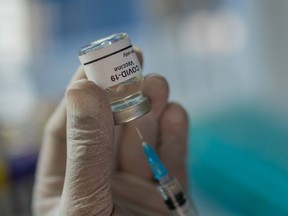 A health care worker wearing gloves and holding a Covid-19 vaccine vial and a syringe - stock photo.
