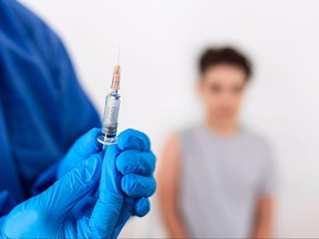 Vaccination. Professional doctor in blue sterile gloves holding syringe and making injection to a little boy wearing medical mask. Immunisation, medicine and healthcare. Covid19, coronavirus vaccine