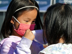 Five-year-old Tessa Ng (left) helps her friend Liv Leong, 5, put on a face mask.