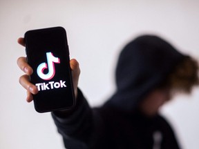 A teenager poses presenting a smartphone with the logo of social network TikTok.