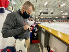 Stratford Warriors trainer Bevan Mathieson makes note of a player's first goal on the milestone puck during the team's first game of the season.