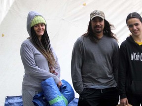 Justin Lewis (centre), along with Patricia Valcourt (left) and Kelvin Boissoneau, stand in front of a white teepee, located on the grounds of the Ronald A. Irwin Civic Centre. Lewis is at the ongoing protest for homelessness and addiction, trying to help people with addiction issues through traditional Indigenous medicines and practices. Lewis says Valcourt and Boissoneau are “like family” as they know each other through Indigenous ceremonies.  Gordon Anderson/Postmedia Network