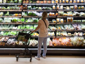 A grocery store shopper inspects a shelf of vegetables wrapped in plastic material.  Getty Images