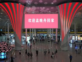 People walk under a giant screen displaying a message that reads "Welcome home Meng Wanzhou" at Shenzhen Baoan International Airport in Shenzhen China September 25, 2021.