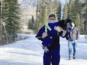 Ryan Strohmaier with the Canmore Fire Department carries a dog named Gonzo who was swimming in the icy cold Bow River, as EPCOR employee Steve Horne walks behind. Steve helped to rescue the dog by coaxing him out of the cold water and wrapping him in his EPCOR jacket. photo by Pam Doyle/www.pamdoylephoto.com